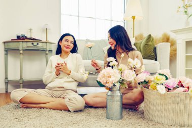 İki Asyalı kadın arasında evde suni çiçekleri düzenlemek için ücretsiz günlük yaşam aktivitesi. Renkli pastel çiçekler ve su içen bayan arkadaş..
