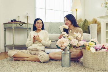 İki Asyalı kadın arasında evde suni çiçekleri düzenlemek için ücretsiz günlük yaşam aktivitesi. Renkli pastel çiçekler ve su içen bayan arkadaş..