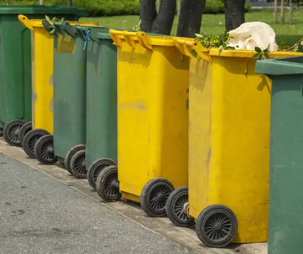 Green and yellow trash cans are located on a walkway in the city park.