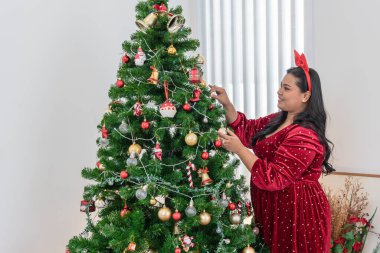 Asyalı bir kadın, Noel arifesinde ve yeni yılda, Noel konsepti için bir aile partisi için güzel bir Noel ağacı süslüyor..