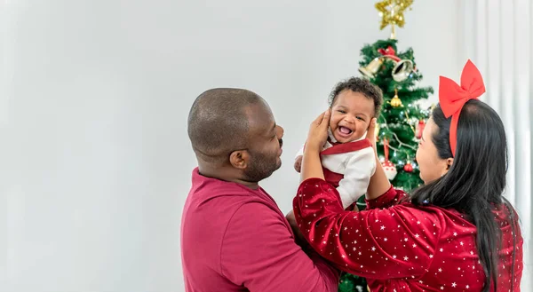 African family, 4-month-old Nigerian baby newborn son, father and mother smiling and happy together, with blur background of Christmas tree, to African family on holiday and baby infant concept.