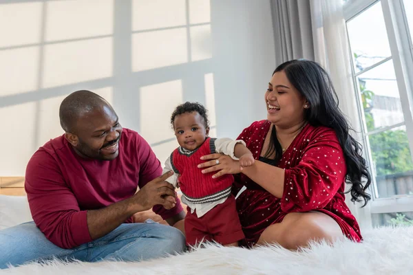 African family, Nigerian father and Asian mother holding a 4-month-old baby newborn son, they are smile and happy together in bedroom. to African family and baby infant concept.