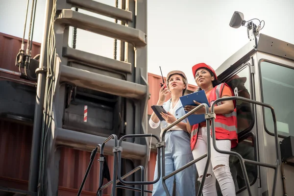 Caucasian engineer woman using a communication radio and African American workers woman, are working in containers industry, logistic transport Import-Export Cargo, to business shipping and warehouse concept.