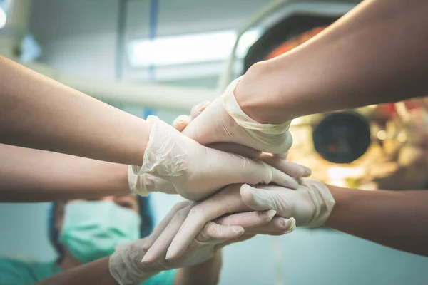 A team of doctors in the operating room join hands of show cooperation and synergy teamwork to be successful in surgical treatment of patients, to health care and teamwork concept.