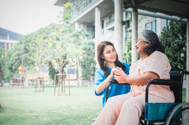 Hastalıkla, yaşlılara sağlık hizmetleri ve osteoporoz kavramına karşı savaşmak için tekerlekli sandalyeye oturmuş yaşlı kadın hastaların elini tutan Asyalı doktor..