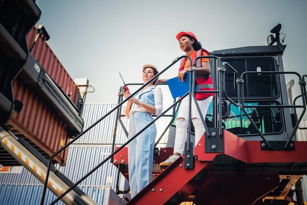 Caucasian engineer woman using a communication radio and African workers woman are working in containers industry, logistic transport Import-Export Cargo, to business shipping and warehouse concept.