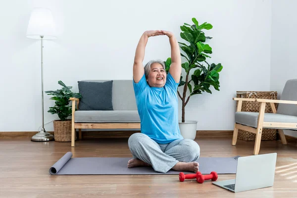 Stock image Asian elderly women are practicing yoga in the basic position in her living room, which is a warm-up and meditation exercise, to elderly health care concept.