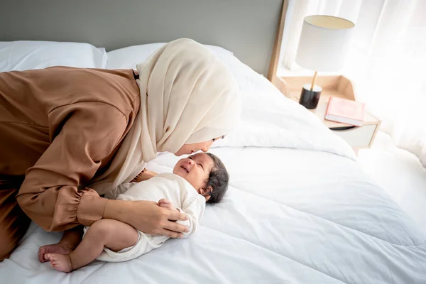 Muslim family, an Asian mother kissing forehead her 1-month-old baby newborn girl, is half Thai-half Nigerian. with happy smile and love, concept to Muslim family and baby newborn