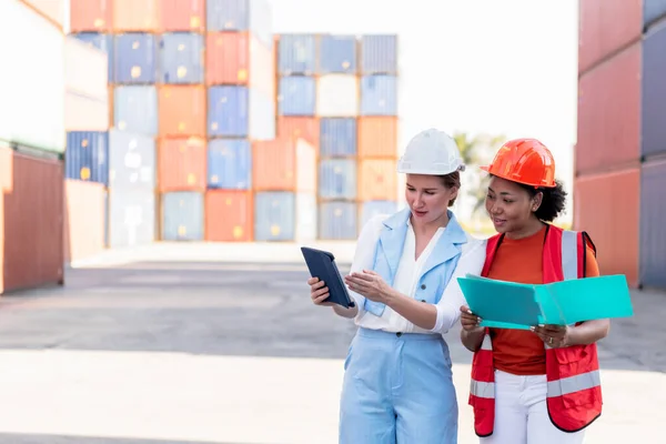 Caucasian female engineer and African worker, are working in containers industry, logistic transport Import-Export Cargo, to business shipping and warehouse concept.