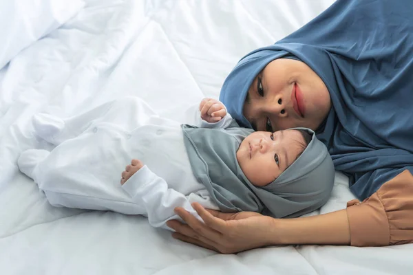 Muslim family, Asian attractive mother and 2-month-old baby newborn girl, is Half-Nigerian Half-Thai, relaxation and lying together on white bed. to relationship in Islamic family and baby concept.
