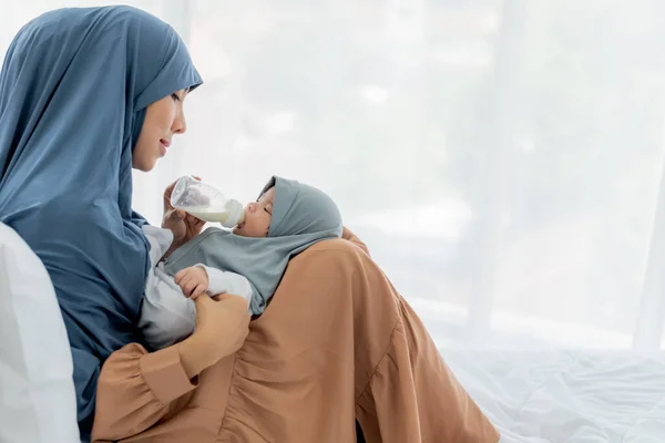 Muslim family, Asian mother feeding milk from bottle milk to her 2-month-old baby newborn girl, is Half-Nigerian Half-Thai, to family and food for infant concept.