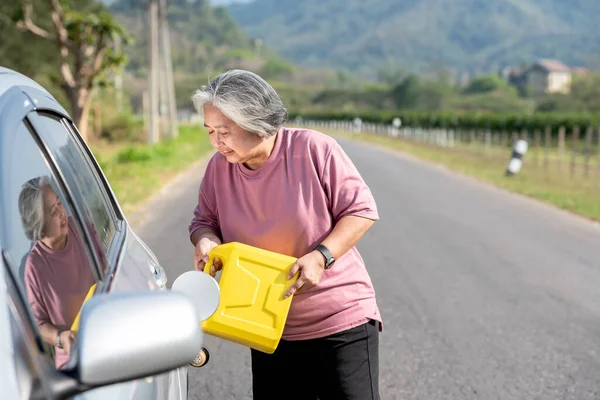 Asian elderly woman holding a Reserve oil tank To refuel the car,  Parked on the roadside, due to the fact that the oil ran out during the journey, to people retirement age  and travel trip concept.