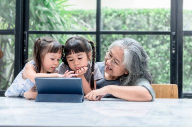 Asyalı aile, yaşlı büyükanne ve iki kız evdeki mermer masada tablete bakıyorlar, bulanık bir geçmişi var, Asyalı aile ve çocuklara çevrimiçi eğitim kavramı.