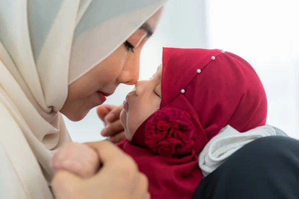 Muslim family, an Asian mother holding and kissing the nose of her 2-month-old baby newborn daughter who is sleeping, with love and happiness. to relationship Muslim family and Islamic children concept.