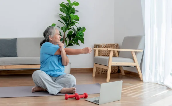 Asian elderly women are practicing yoga in the basic position in her living room, which is a warm-up and meditation exercise, to elderly health care concept.