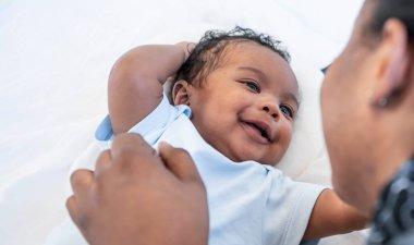 an African newborn baby is 2 months old lying on a white bed smiling happily When he is looking at his mother, to relationship in African family and black newborn concept.