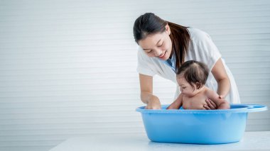 Asian mother Bathing her 7-month-old daughter, which the baby smiling and happy, with white background. to Asian family and baby shower concept.