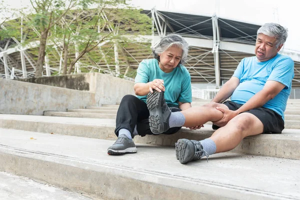 Asian elderly couple, wife squeezing and stretching her husband\'s leg muscles with injuries, cramps from exercise. to people retirement age and muscle cramp concept.