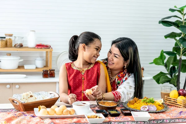 an Indian family, mother and daughter in the kitchen They happy together while eating Indian food, placed on the table, to family and Indian food concept.