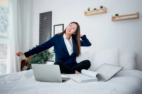 Asian businesswoman attractive and young, sitting and working on white bed, and doing stretching to loosen her muscles to reduce fatigue form work. to working hard for job success cocnept.