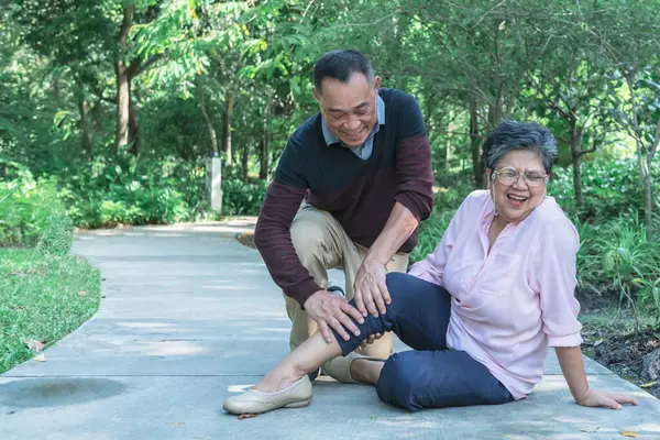 Asian elderly couple, The husband is massaging his wife\'s calves and legs, who is having cramps, while a retired couple walking in the park. to health care and elderly couple concept.