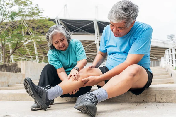 Asian elderly couple, wife squeezing her husband\'s leg muscles with injuries cramps from exercise. to people retirement age health care and muscle cramp concept.