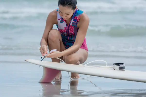 Asian woman surfer wear water exercise clothes attaching the ankle strap to the surfboard. for safety while surfing in the sea. to people sport recreation and protective equipment in sports concept.