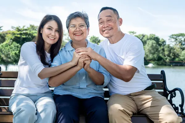 Asian family, Elderly parents and daughter sitting on chair in the park, they holding hands to show their love, relationship and encourage each other in the family.