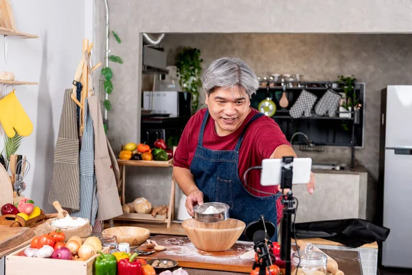 Asian fat man standing in the kitchen, preparing equipment to make content about pizza homemade. to Influencer Marketing and social media concept.