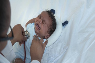 Steteskop kullanan Afrikalı bir doktor, 12 günlük bir bebeğin kalp atışlarını ve solunum sistemini kontrol ediyor. Bebek siyahi tenine ve sağlık konseptine uzanan ve ağlayan yeni doğmuş bir bebeğin.