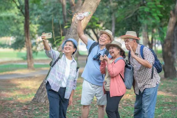 A group of Asian tourists use their cell phones to take selfies together in a forest park. Smiling and laughing happily Ideas for traveling in retirement