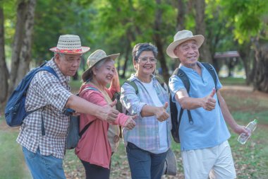 Asyalı turistler, yaşlı erkekler ve kadınlar bir sırt çantası alıp orman parkında doğa gezintisine çıkarlar. Birlikte başparmağımızı sallar ve şükranla gülümseriz..