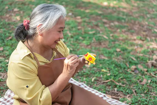 Elderly woman doing activities in the park Use a paintbrush to paint pottery. learn art to treat depression The concept of depression in the elderly