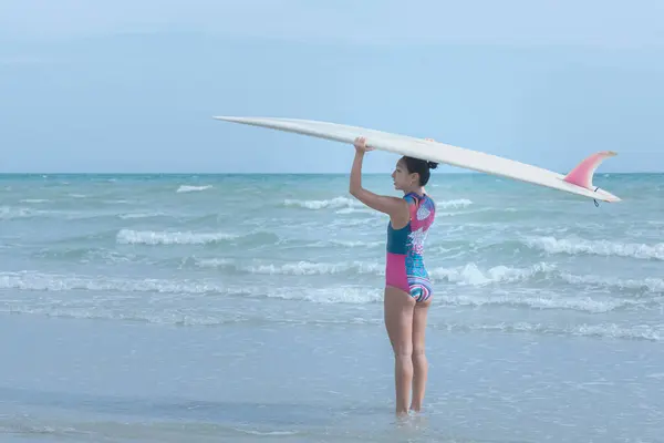 Asian woman wearing water sports suit holding a surfboard and walking into the sea to surf. to people sport recreation and exercise by surf in the sea concept.