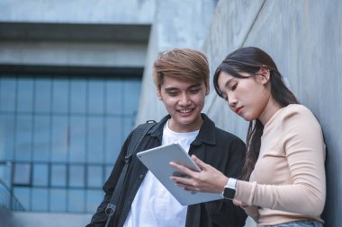 Asyalı kadın ve erkek öğrenciler, insanlar ve yetişkin eğitim kavramları hakkında dersler almak için bilgisayar notlarına bakıyor ve onları kullanıyorlar..