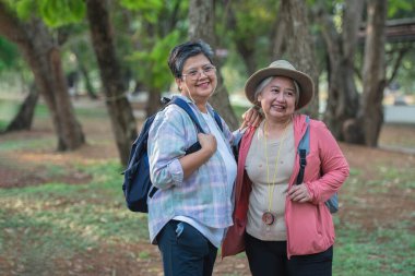 Asyalı turistler bir sırt çantası alıp Tayland 'ın orman parklarından birinde doğada dolaşırlar. Emeklilikte tatile gitme kavramı.