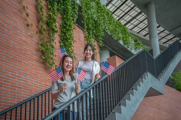Duas Estudantes Universitárias Asiáticas Estão Segurando Bandeiras Americanas Nas Escadas Fotografias De Stock Royalty-Free