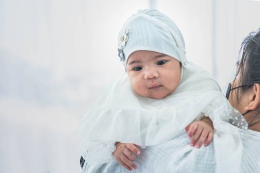 Müslüman bir aile, Asyalı bir anne kucağında yeni doğmuş bir kız çocuğu iki aylık. Beyaz arka planda duruyor. Müslüman aileye ve yeni doğan bebek kavramına.