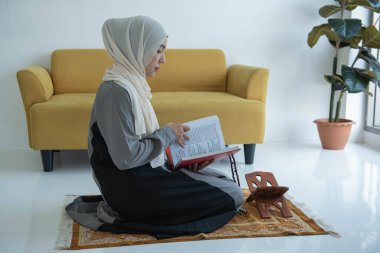 A Muslim sits on a carpet and reads the Islamic Quran that Muslims believe is given by God. To individuals and faith in Islam clipart