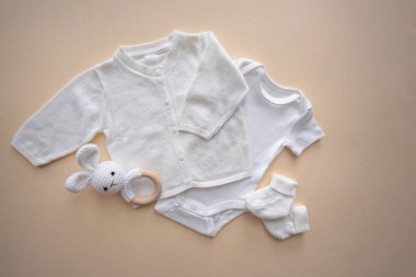 Beyaz bebek kıyafetleri, aksesuarlar ve kahverengi arka planda oyuncaklar. Yeni doğmuş vücut, şapka ve çoraplar. Yeni doğan temel ihtiyaçlar ve annelik kavramı. Yüksek kalite fotoğraf