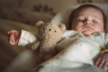 Uyuyan yeni doğmuş bebek battaniyenin altında yumuşak bir oyuncak ayıyla yatıyor. Çocukluk ve ebeveynlik kavramı. Yüksek kalite fotoğraf