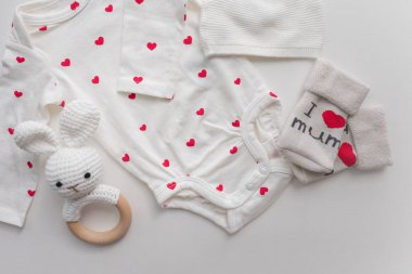 Beyaz bebek kıyafetleri, kırmızı kalpler, aksesuarlar ve beyaz arka planda oyuncaklar. Yeni doğmuş vücut, şapka ve çoraplar. Bebek gereksinimleri ve annelik kavramı. Yüksek kalite fotoğraf