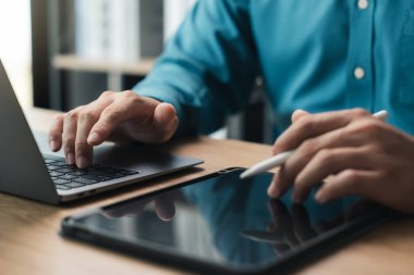 Bir adam dizüstü bilgisayarda ve tablette yazıyor. Tablete yazmak için bir stil kullanıyor. Verimlilik ve odaklanma kavramı, adam hem bir dizüstü hem de bir tablet gerektiren bir görev üzerinde çalışıyor.