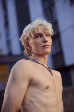 A shirtless teenage boy is posing on the street surrounded by buildings.