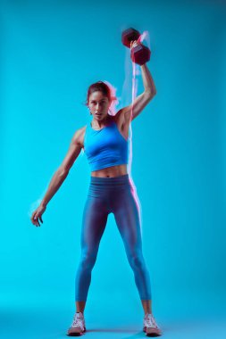Stüdyoda dambılı kaldıran bir kadın vücut geliştirici. Uzun pozlama hareketi yakalaması.