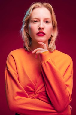 Portrait of a serious young blond woman in yellow sweatshirt isolated on magenta background. Viva magenta.