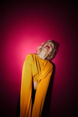 A young blond woman standing in front of the magenta background. Viva magenta.