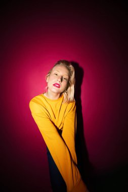 Portrait of a serious young blond woman in yellow sweatshirt isolated on magenta background. Viva magenta.