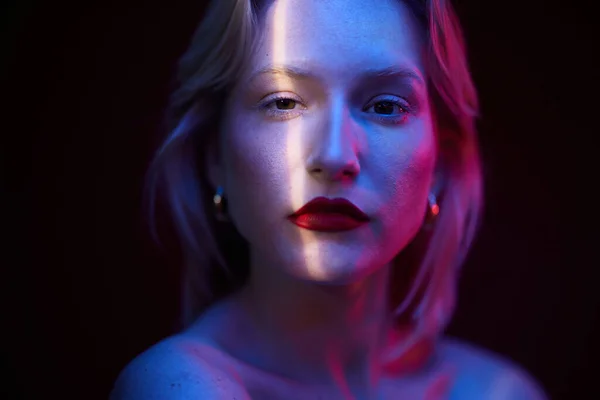 Portrait of a woman looking at the camera. There is a light on her face. Photo gel, blue and magenta. Viva magenta.
