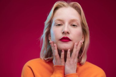 Portrait of a serious young blond woman in yellow sweatshirt isolated on magenta background. Viva magenta.